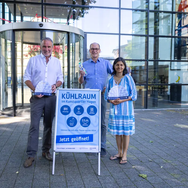 Foto: Die in der Bildzeile genannten Personen stehen hinter einem Auftsellschild mit Informationen zur K&uuml;hloase vor dem Osthausmuseum und halten Flyer und eine Wasserflasche in die H&ouml;he.