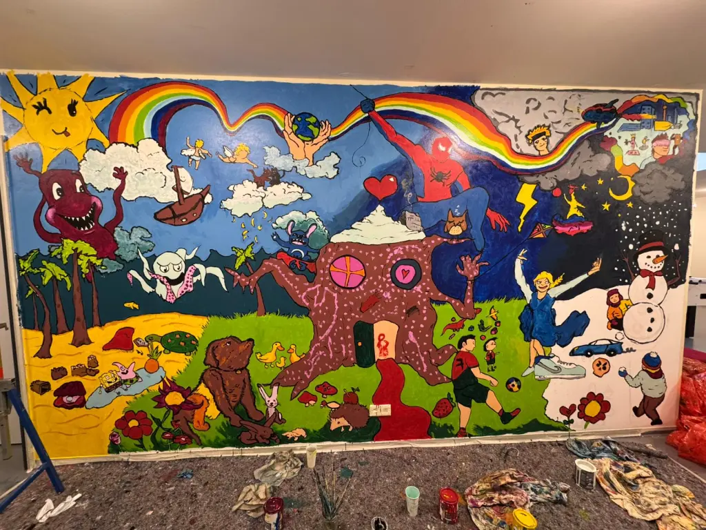 Foto: Eine Wand mit vielen bunten Kunstwerken, z.B. ein Regenbogen, ein Haus, Tiere und verschiedene Comcic- bzw. Zeichentrickfilmhelden