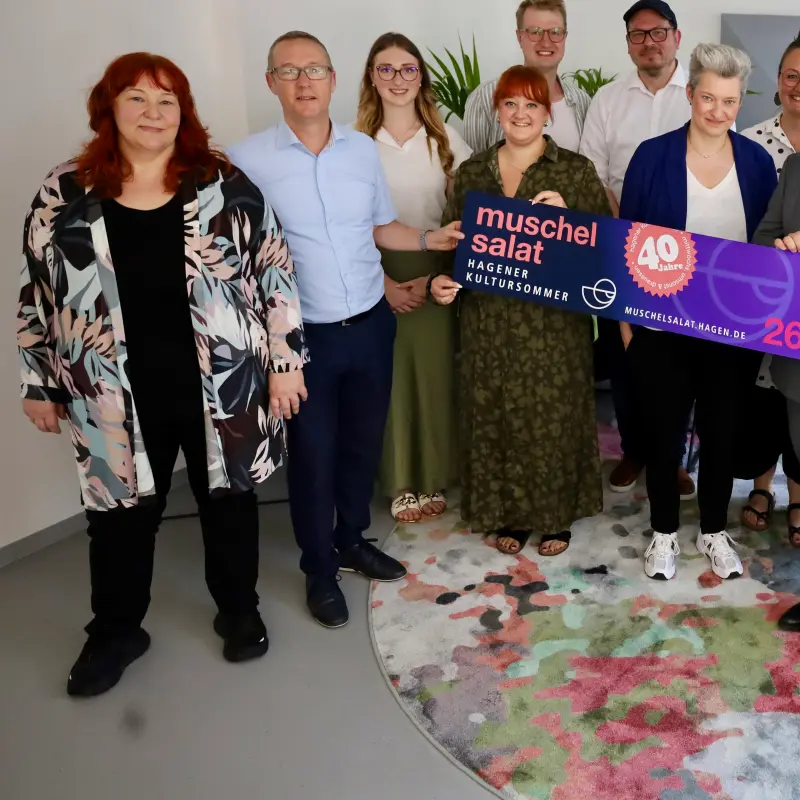 Foto: Die oben genannten Personen halten ein Banner in den H&auml;nden, auf dem Werbung f&uuml;r den 40. Muschelsalat gemacht wird.