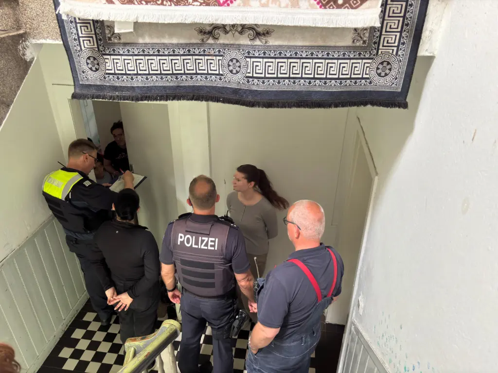 Foto: Mitarbeiter von Polizei und Ordnungsamt stehen zusammen mit Bewohnerinnen im Flur eines Hauses.