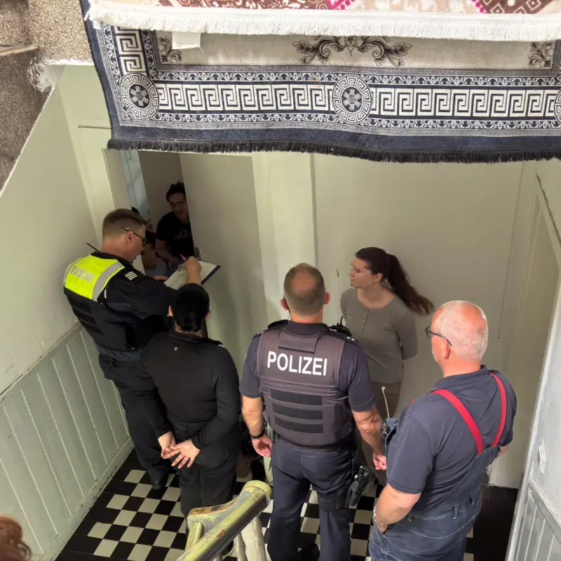 Foto: Mitarbeiter von Polizei und Ordnungsamt stehen zusammen mit Bewohnerinnen im Flur eines Hauses.