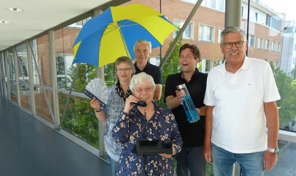 Foto: Das Team des Hitztelefons Hagen steht nebeneinander und haben einen Schirm eine Wasserflasche, ein Telefon und einen Informationsflyer in der Hand.