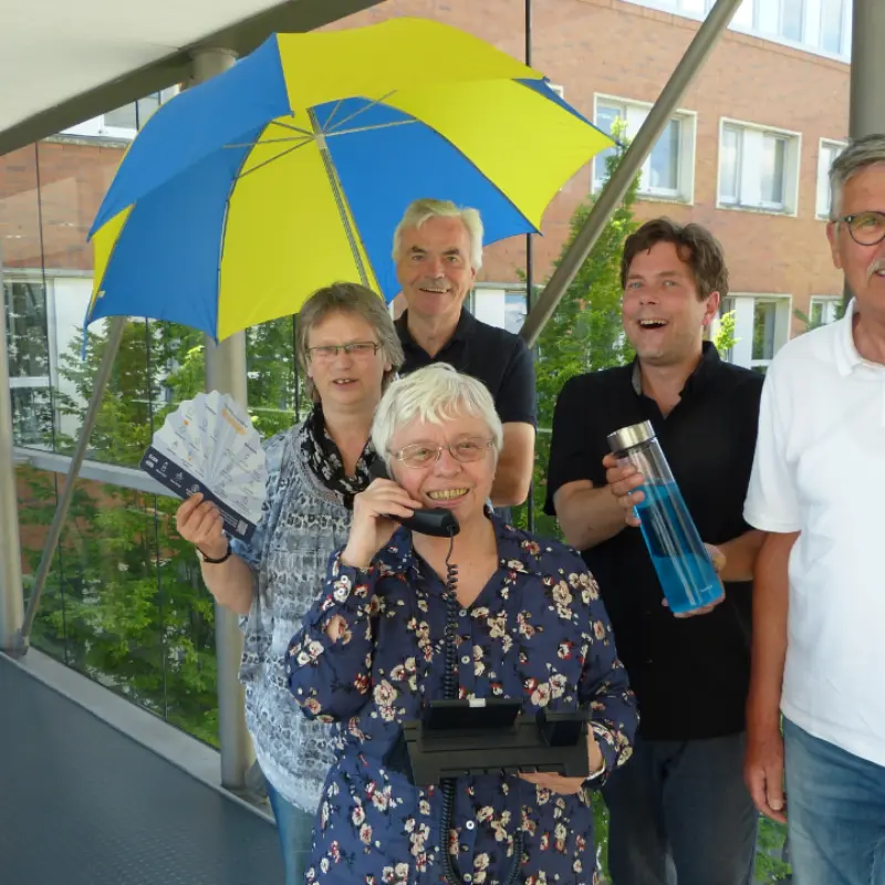 Foto: Das Team des Hitztelefons Hagen steht nebeneinander und haben einen Schirm eine Wasserflasche, ein Telefon und einen Informationsflyer in der Hand.