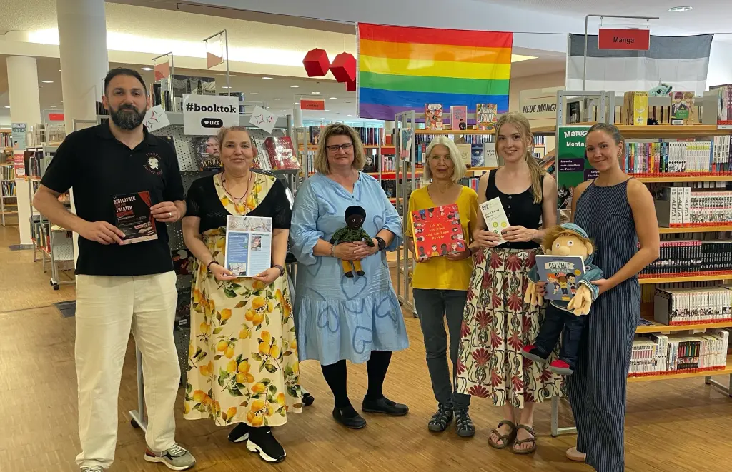 Foto: Die in der Bildzeile gennnten Personen stehen nebeneinader und halten B&uuml;cher sowie Kuscheltiere in den H&auml;nden.