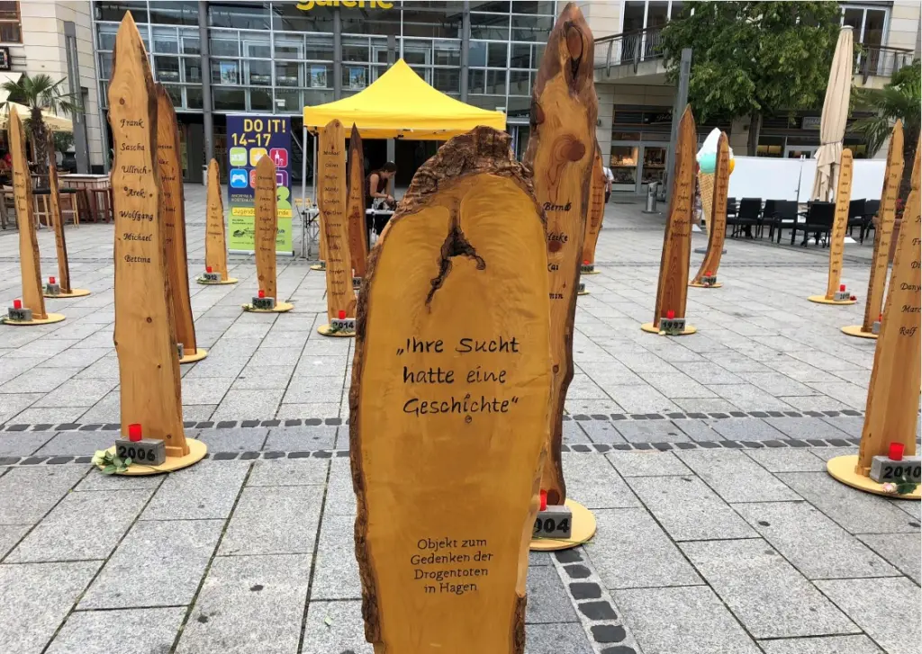 Foto: Holzstelen, auf denen Namen notiert wurden. Darunter steht in Stein eingemei&szlig;elt jeweils ein Jahr. Auf einer Stele setht "Ihre Sucht hatte eine Geschichte" - Objekt zum Gedenken der Drogentoten in Hagen.