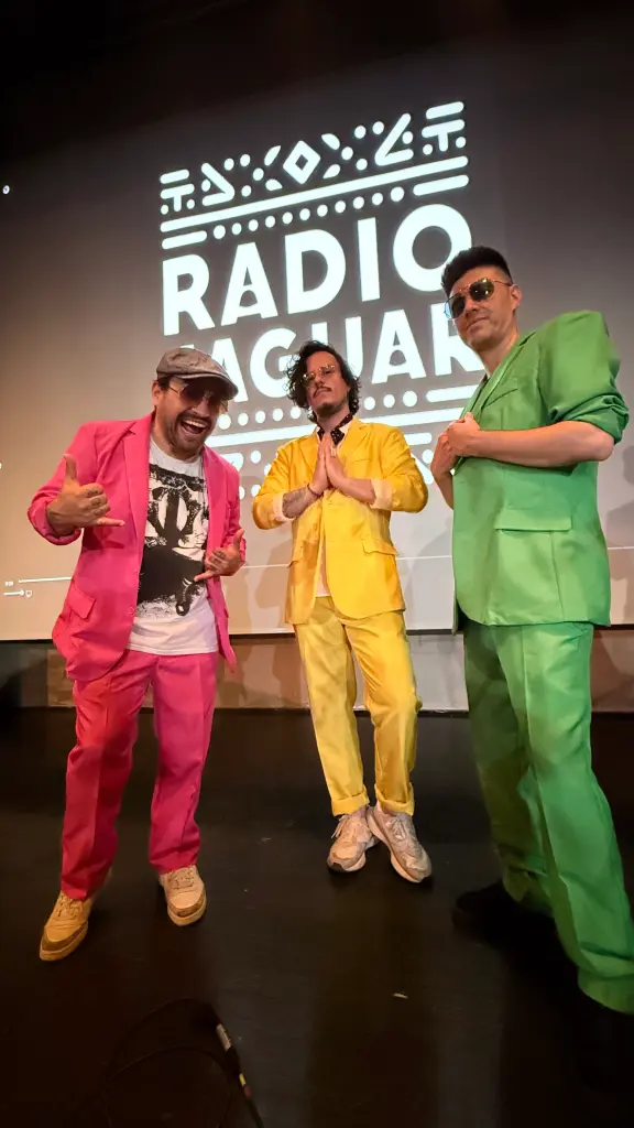 Foto: Die Bandmitglieder haben knallbunte Anzüge an und stehen vor einer Wand, auf der "Radio Jaguar" steht.