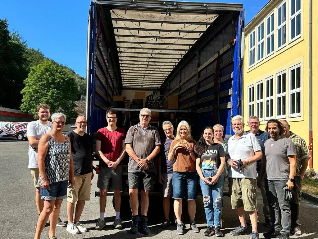 Foto: Die an der Aktion Beteiligten stehen vor einem LKW, in dem sich die Schulmöbel befinden.