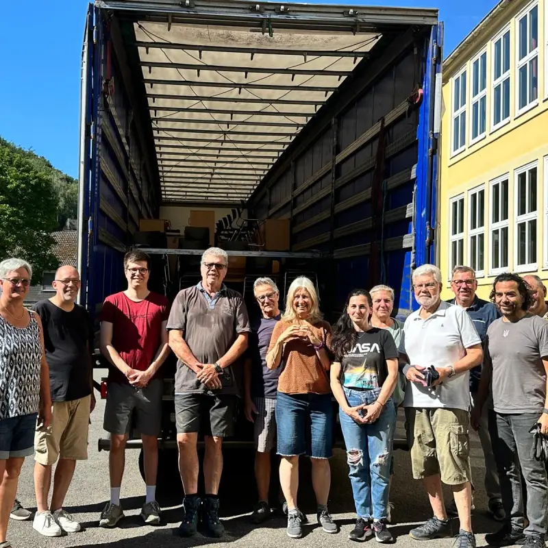 Foto: Die an der Aktion Beteiligten stehen vor einem LKW, in dem sich die Schulmöbel befinden.