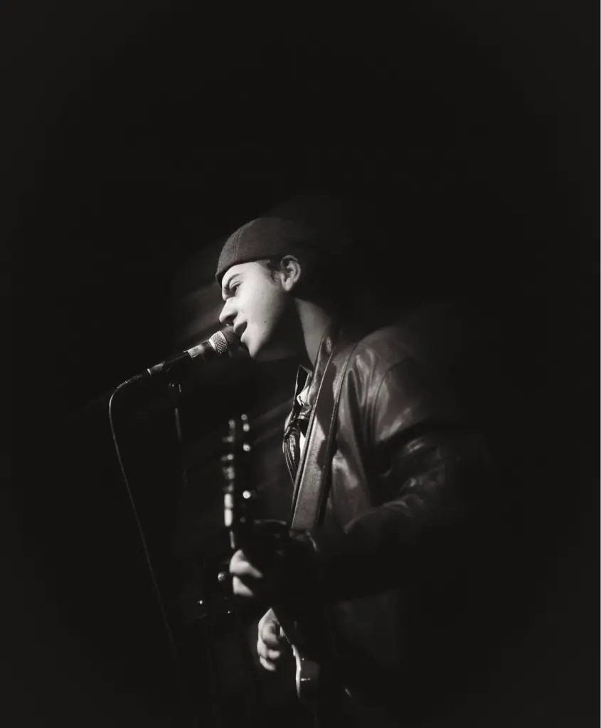 Foto: Der Sänger Seydin steht mit einer Gitarre in der Hand vor einem Mikrofon und singt.