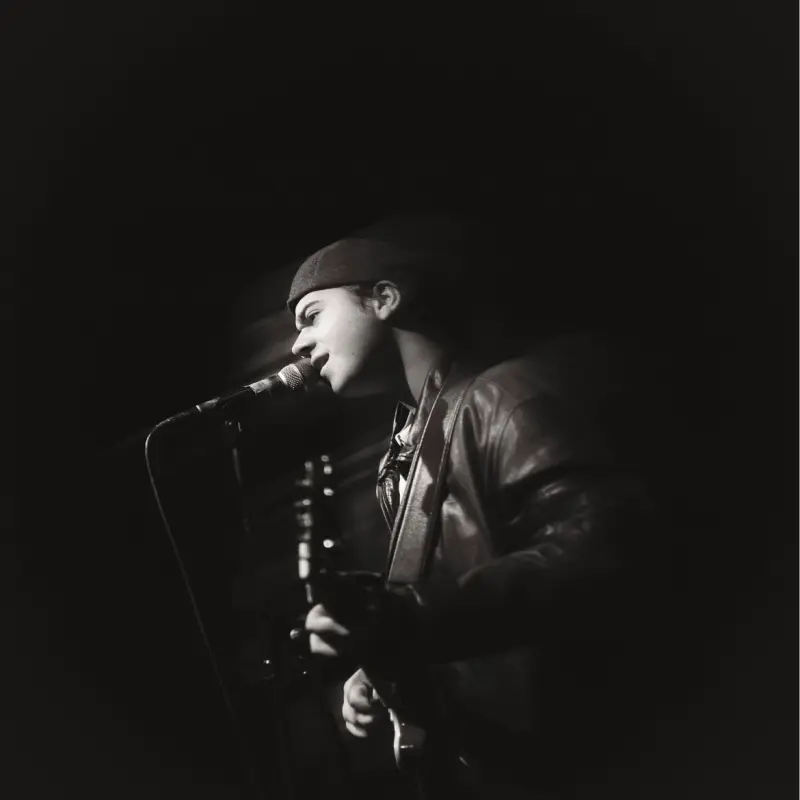 Foto: Der Sänger Seydin steht mit einer Gitarre in der Hand vor einem Mikrofon und singt.