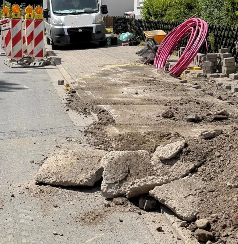 Foto: Baustellenbaken, dahinter ein Transporter. Im Vordergrund liegen Asphaltplatten.