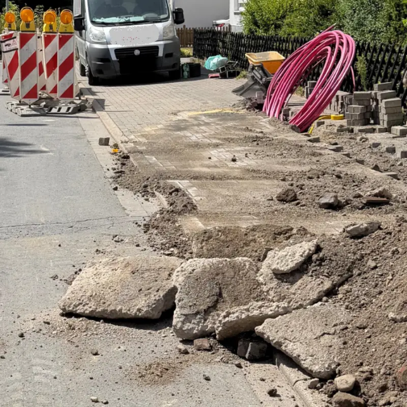 Foto: Baustellenbaken, dahinter ein Transporter. Im Vordergrund liegen Asphaltplatten.