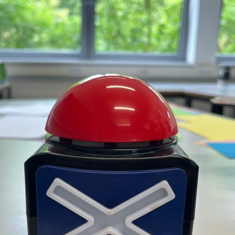 Foto: Ein roter Buzzer mit einem Kreuz an der Seite steht auf einem Tisch.
