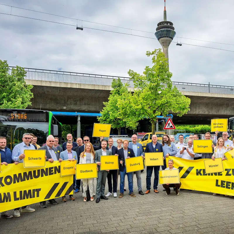 Foto: Vertreter der Kommunen stehen vor einem Bus, einer Kehrmaschine, einem Feuerwehrauto und halten Schilder mit Ortsnamen hoch sowie Banner mit der Aufschrift "Kommunen am Limit" sowie "Keine Zukunft mit leeren Kassen"