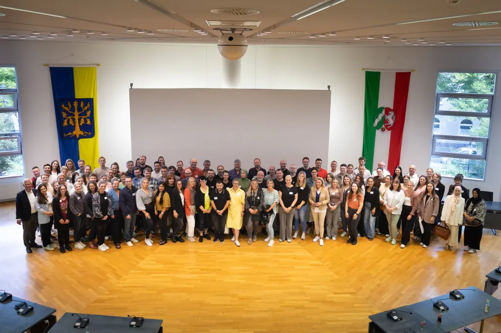 Foto: Eine sehr große Gruppe an Menschen, die von oben fotografiert wurde und in einem großen Saal steht.