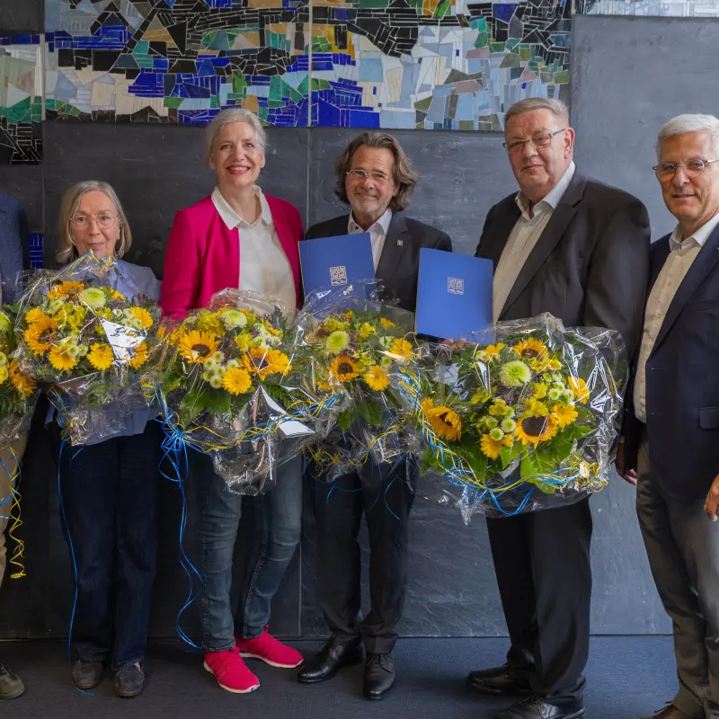 Foto: Drei Männer und drei Frauen in schicker Kleidung lächeln in die Kamera. Bis auf einen halten alle Personen einen Blumenstrauß in der Hand.