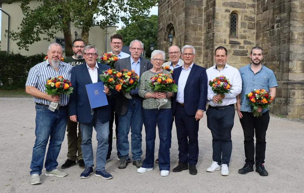Fotos: Viele Personen stehen nebeneinander, teilweise mit Blumensträußen in der Hand, und lächeln in die Kamera.