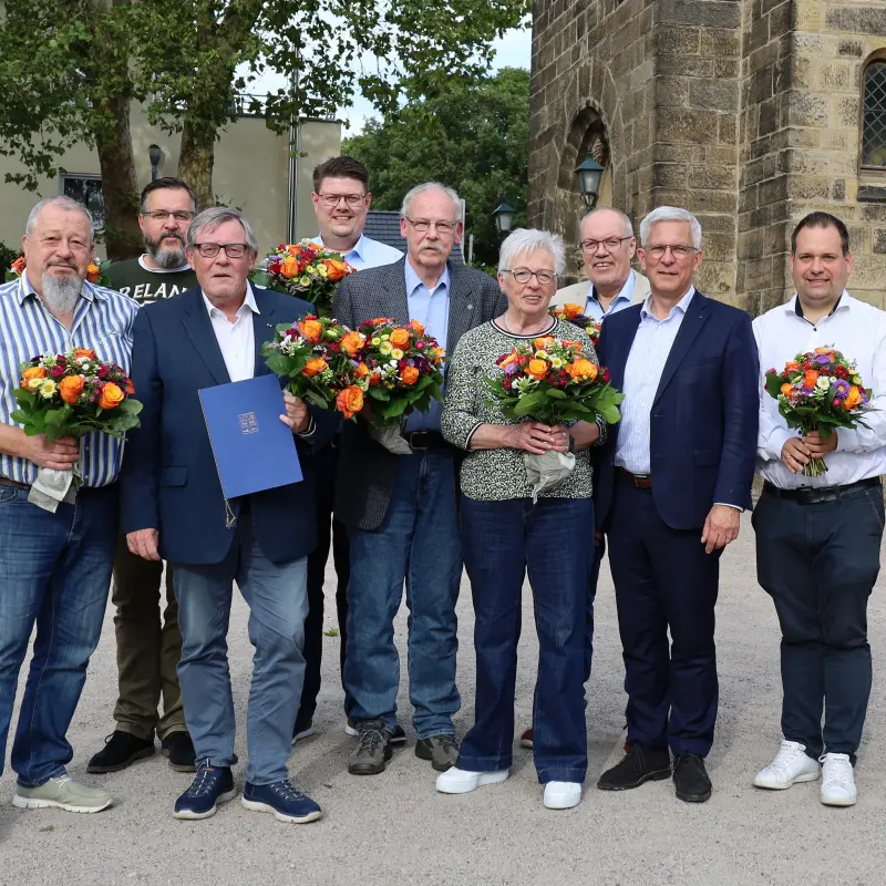 Fotos: Viele Personen stehen nebeneinander, teilweise mit Blumensträußen in der Hand, und lächeln in die Kamera.