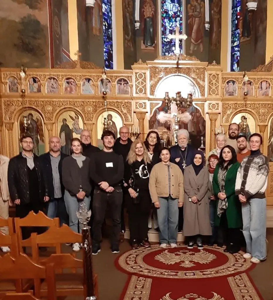 Foto: Mehrere Personen stehen gemeinsam mit einem Priester in einer stark geschm&uuml;ckten Kirche und l&auml;cheln in die Kamera.