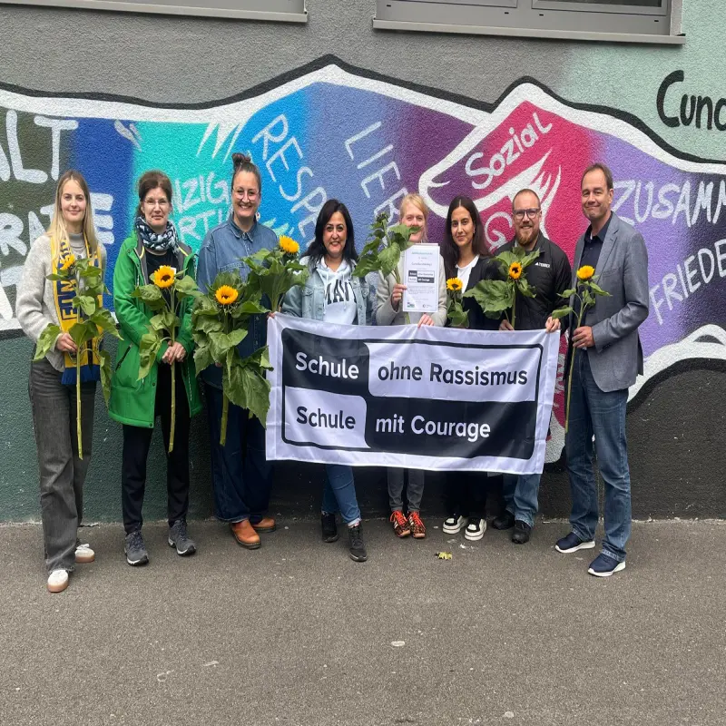 Mehrere Personen posieren für die Kamera und präsentieren das Banner mit der Aufschrift „Schule ohne Rassismus – Schule mit Courage“.