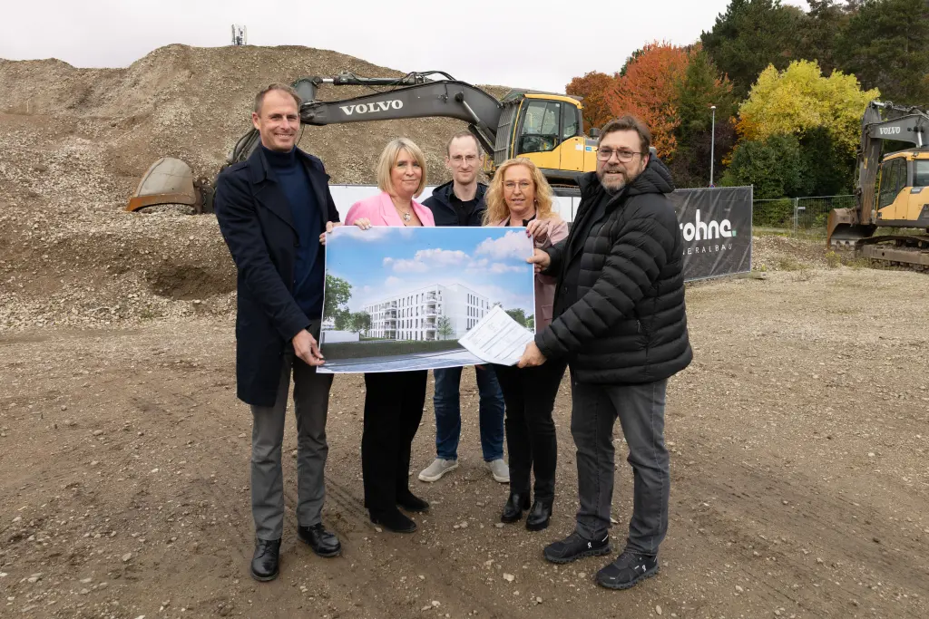 Foto: Die Beteiligten halten einen Geb&auml;udeplan und l&auml;cheln in die Kamera.