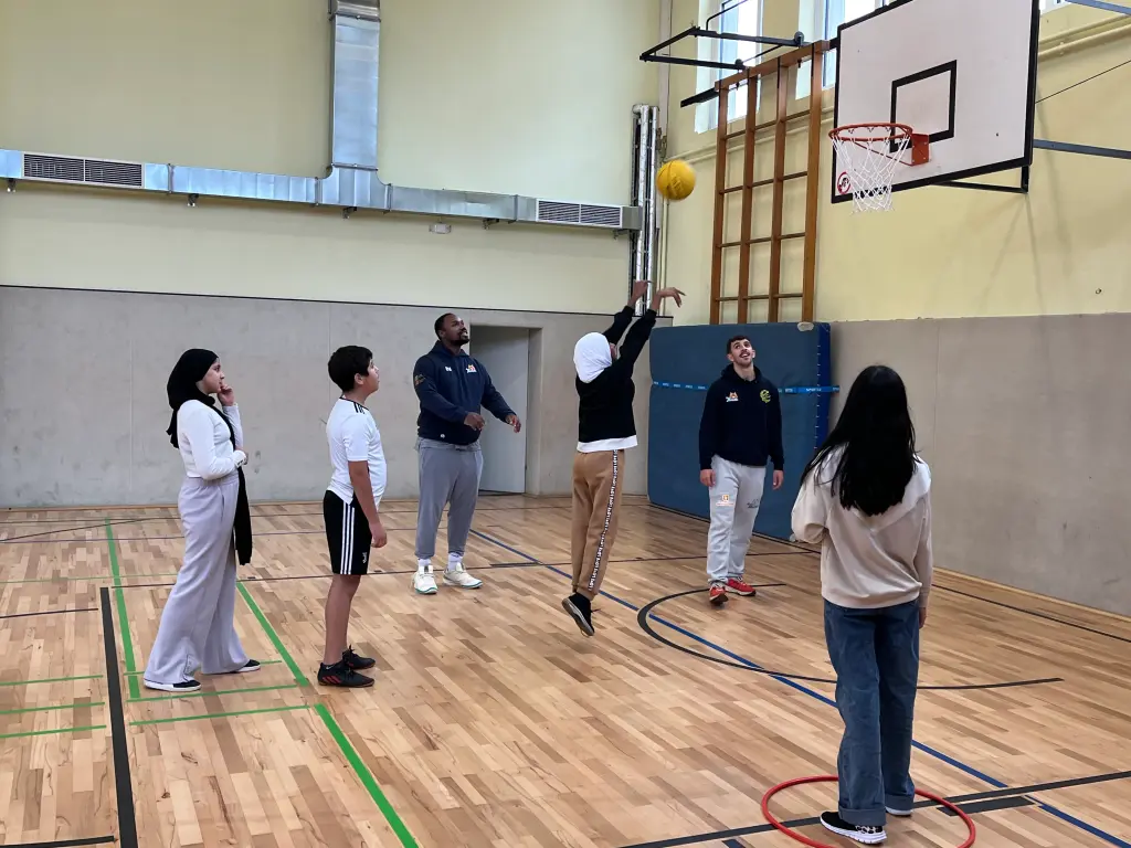 Foto: Mehrere Jugendliche spielen zusammen Basketball in einer Turnhalle.