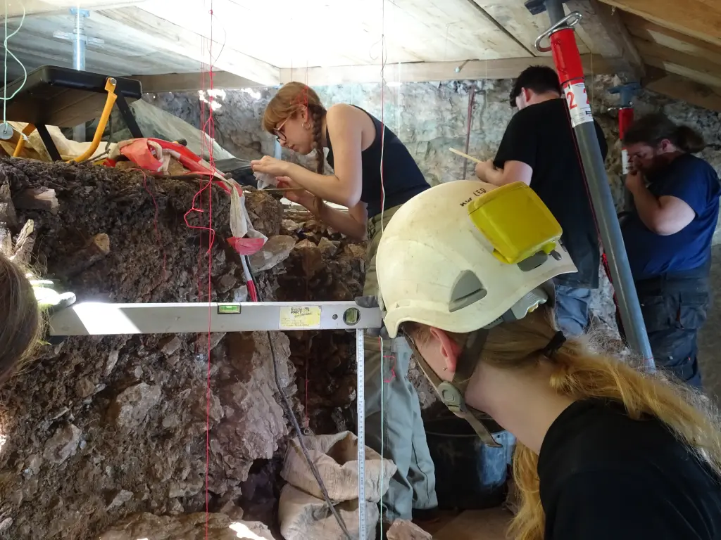 Foto: Mehrere junge Menschen in Arbeitskleidung untersuchen das Gestein in der Blätterhöhle.