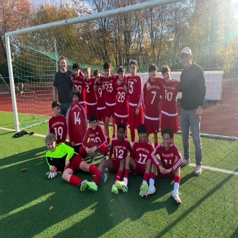 Foto: Ein Fußballteam mit roten Trikots steht jubelnd in einem Fußballtor.