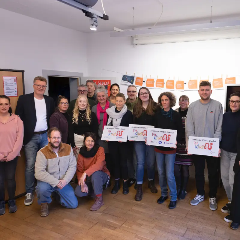 Foto: Mehrere Menschen stehen nebeneinander, vier von Ihnen halten Exemplare des Fitkids-Siegels in den Händen.
