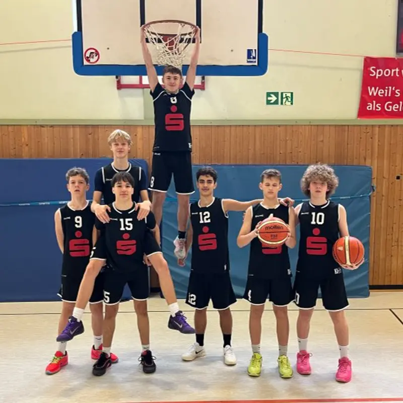 Foto: Sieben Jugendliche in Basketballkleidung stehen auf dem Basketballfeld unter dem Korb und schauen in die Kamera.