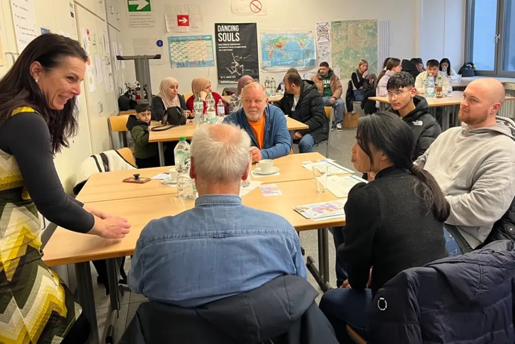 Foto: Vassiliki Kasdanastassi im Gespräch mit mehreren Personen an einem Tisch in einem Klassenzimmer.