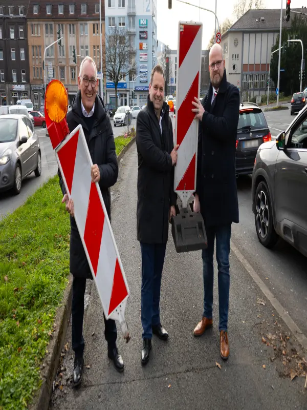 Foto: Regierungspräsident Heinrich Böckelühr, Oberbürgermeister Dennis Rehbein und Bezirksbürgermeister Tobias Fischer halten zwei Absperrbaken in den Händen.