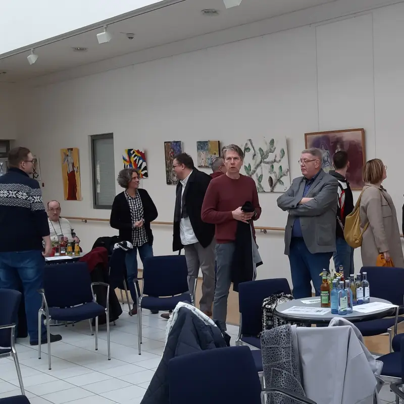 Foto: Zu sehen sind mehrere Personen in einem Gro&szlig;en Raum. An der Wand h&auml;ngen Bilder der Ausstellung.