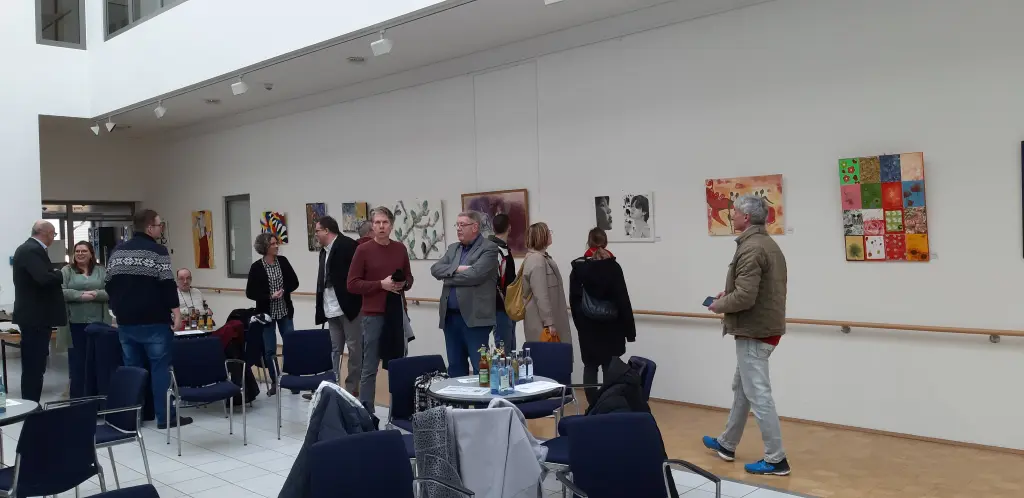 Foto: Zu sehen sind mehrere Personen in einem Großen Raum. An der Wand hängen Bilder der Ausstellung.