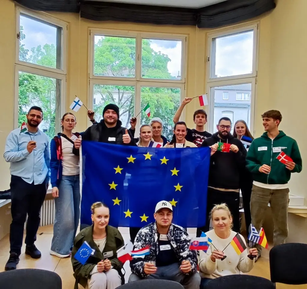 Gruppenfoto: Mehrere Sch&uuml;ler posieren mit einer gro&szlig;en EU-Flagge und vielen kleinen L&auml;nderflaggen.