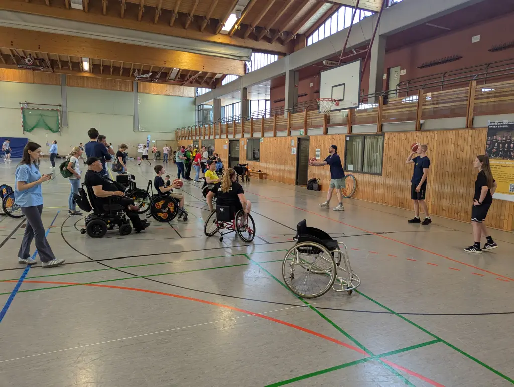 Foto: Personen mit einer Gehbehinderung spielen Basketball in einer Sporthalle.