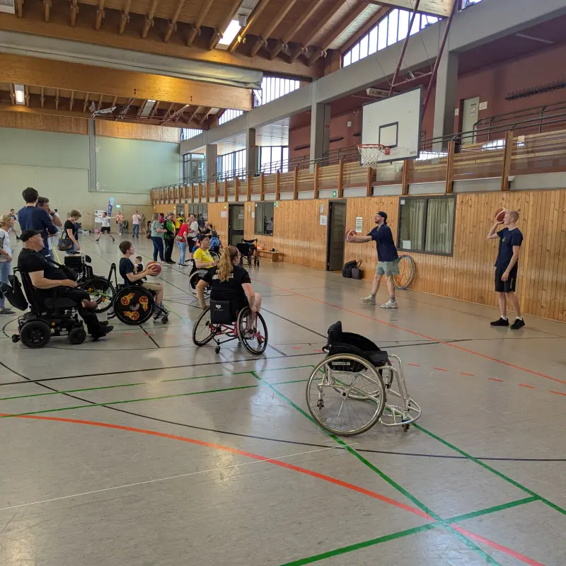 Foto: Personen mit einer Gehbehinderung spielen Basketball in einer Sporthalle.