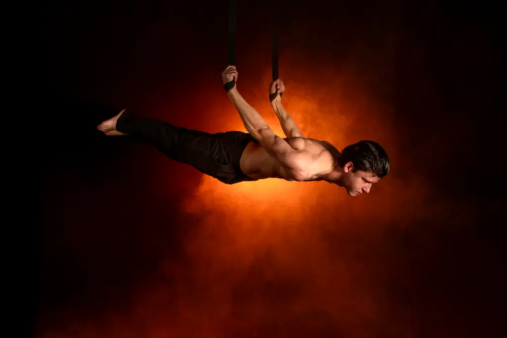 Foto: Ein Artist hängt in einer waagerechten Position mit den Armen nach hinten gestreckt an zwei Seilen.