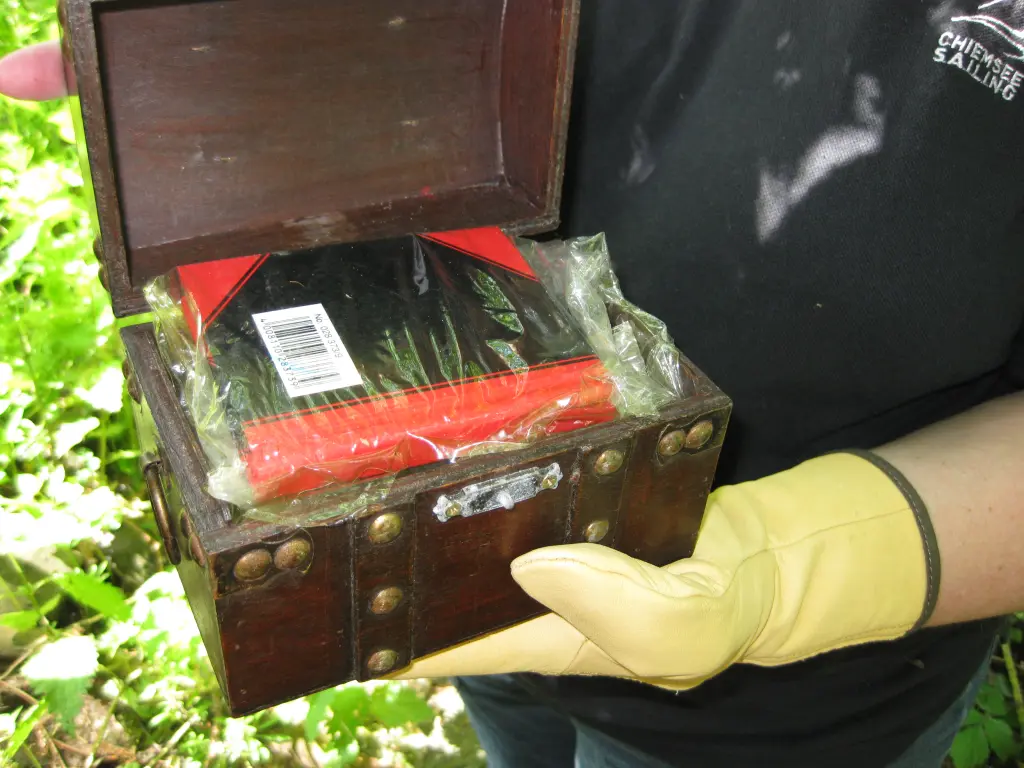 Foto: Ein Geocacher h&auml;lt eine Schatztruhe mit einem Buch in den H&auml;nden.