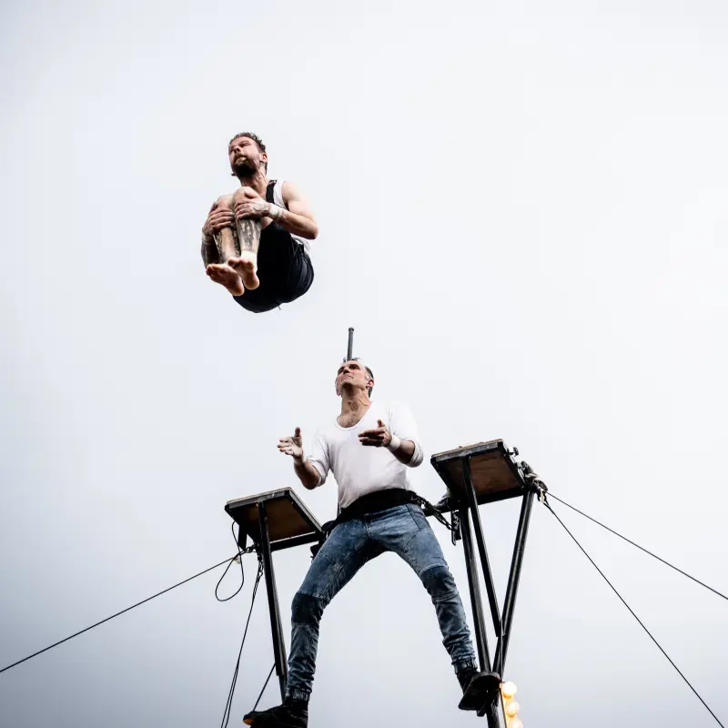Foto: Ein Artist springt in einer eingerollten Position von einem Podest.