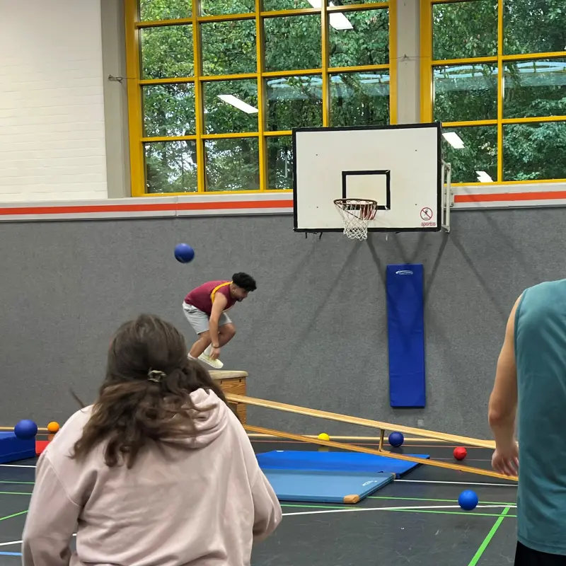 Foto: Ein Schüler wirft einen Ball auf einen anderen Schüler, der den Parcours durchläuft.
