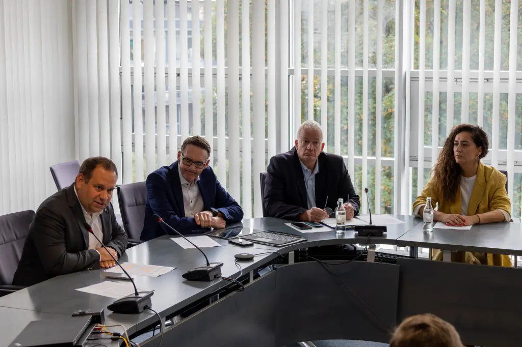 Foto: Die vier im Bildtext genannten Personen sitzen an einem Konferenztisch.