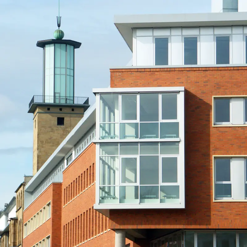 Foto: Die Ecke eines Gebäudes mit einer Turmspitze im Hintergrund.