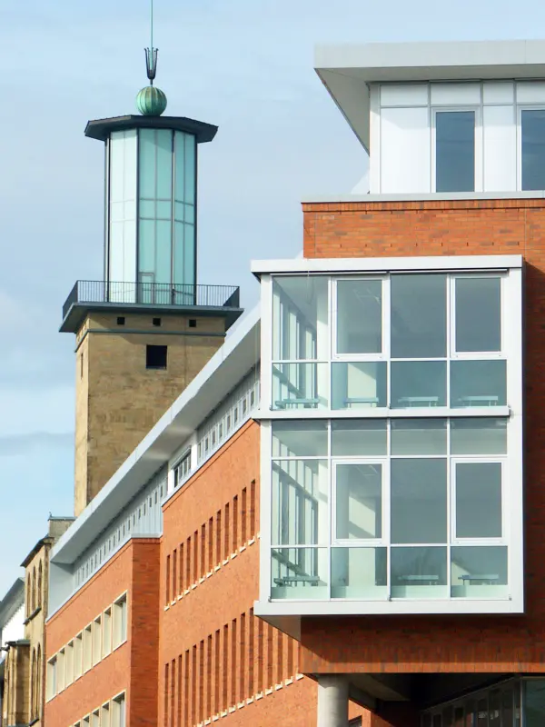 Foto: Die Ecke eines Gebäudes mit einer Turmspitze im Hintergrund.