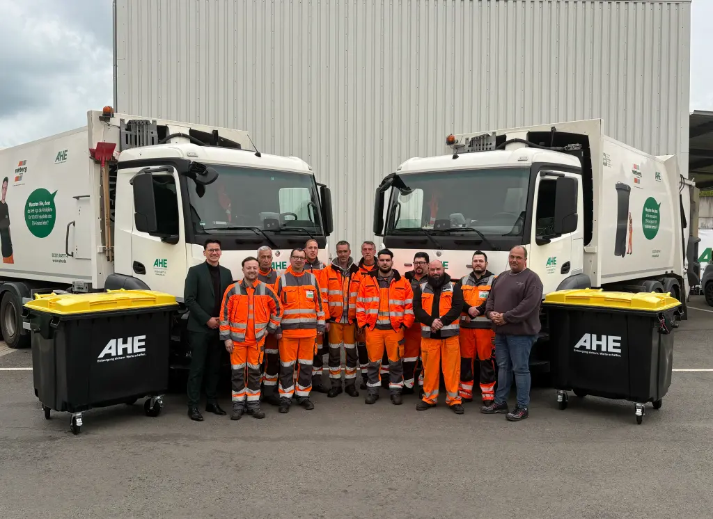 Foto: Gruppenbild von AHE-Mitarbeitenden mit Wertstofftonnen und Fahrzeugen.