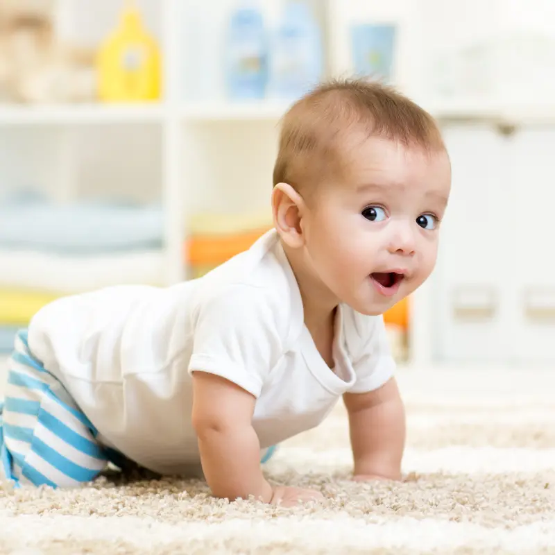 Foto: Ein gl&uuml;ckliches Baby krabbelt in einem Zimmer &uuml;ber einen Teppich.