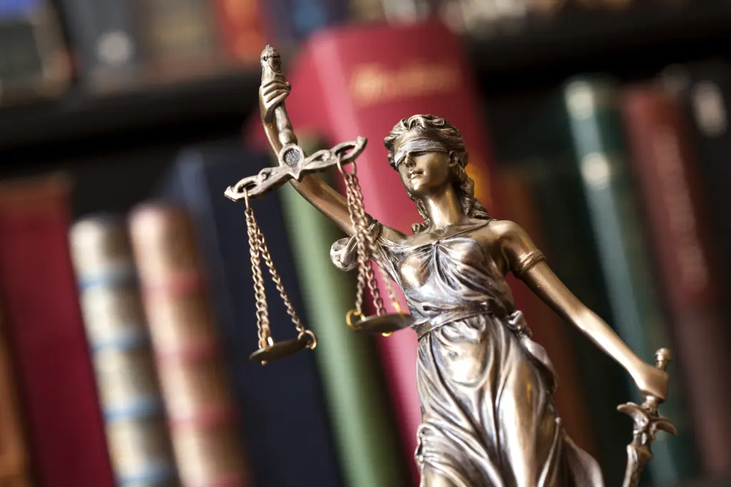 Foto: Eine kleine Bronzestatue von Justizia mit verbundenen Augen einer Waage in der Hand.