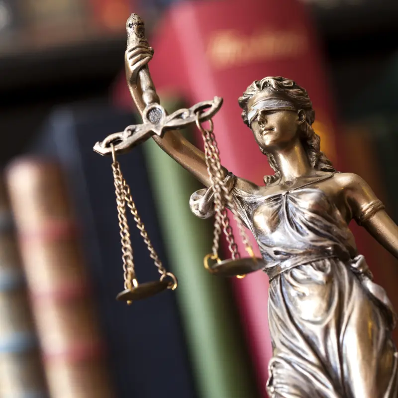 Foto: Eine kleine Bronzestatue von Justizia mit verbundenen Augen einer Waage in der Hand.