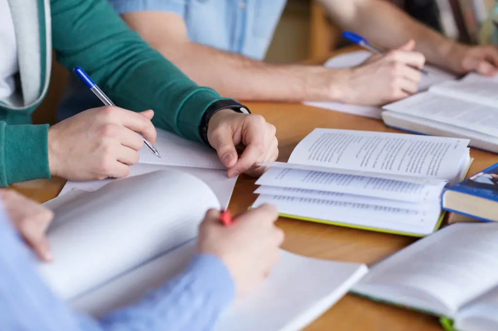 Foto: Mehrere Menschen sitzen an einem Tisch und lernen mit aufgeschlagenen Büchern.