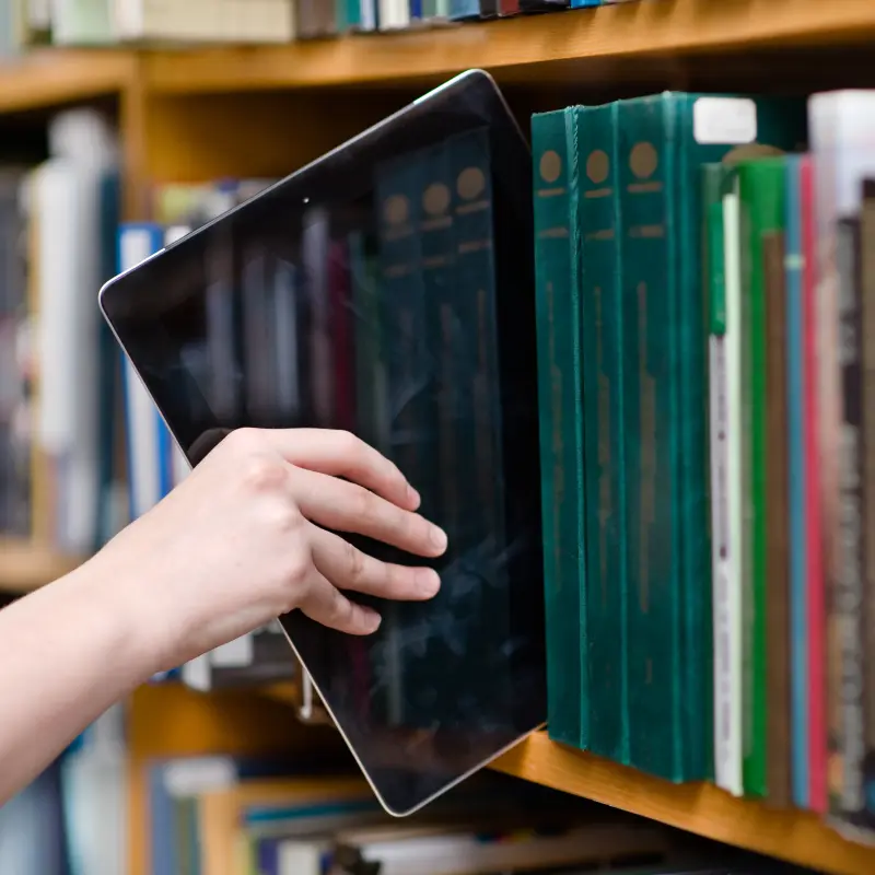 Foto: Ein Tablet wird aus einer Reihe von B&uuml;chern herausgezogen.
